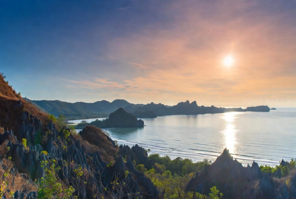 Panorama senja di atas bukit Karst Papua yang memantulkan cahaya keperakan di permukaan laut