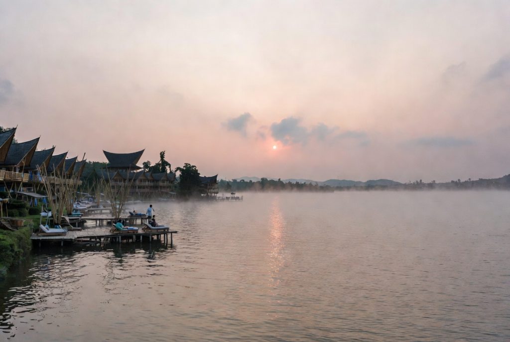Seseorang sedang melakukan meditasi atau yoga di dek kayu tepi danau dengan latar belakang perbukitan Samosir yang berkabut
